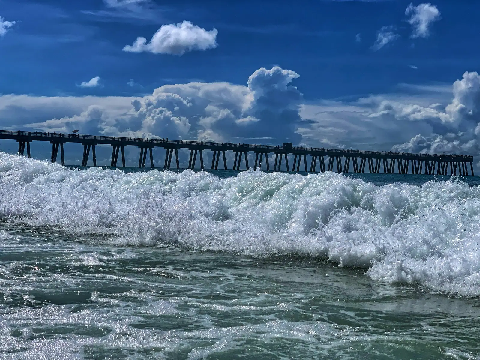 Surf rolling in beside the Navarre Beach pier under a blue sky
