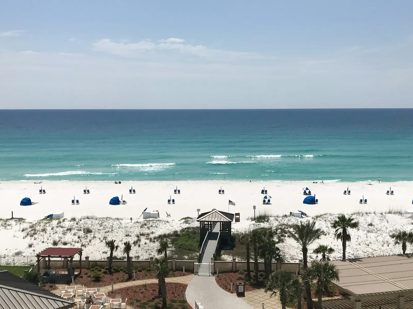 Boardwalk, palm trees and blue beach umbrellas on white sand near Gulf Breeze